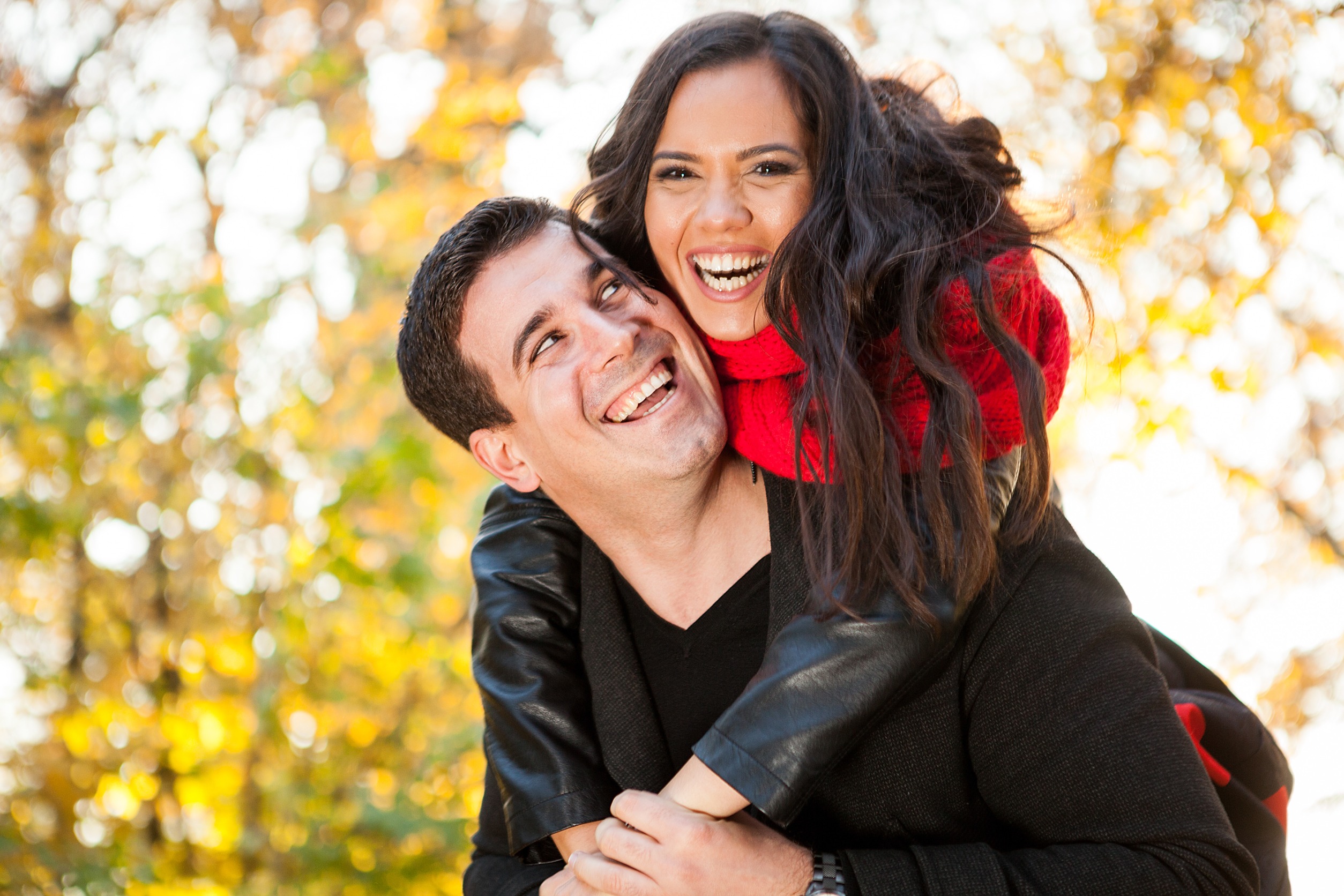 Image of a smiling woman sitting on a smiling man's back outside. Discover how couples therapy in Denver, CO can help you and your partner effectively communicate your needs.